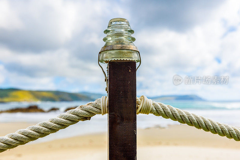 沙滩上木柱上的绳索围栏和玻璃灯。