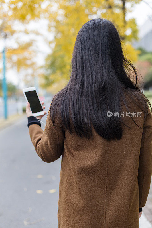 女人在城市街道上拿着智能手机的后视图