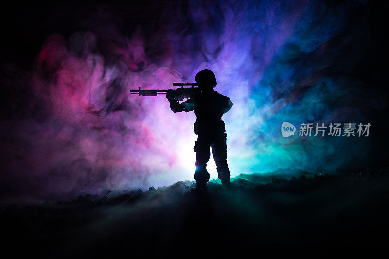军事狙击手的剪影与狙击枪在黑暗色调的雾背景。开枪，拿着枪，五彩的天空，背景