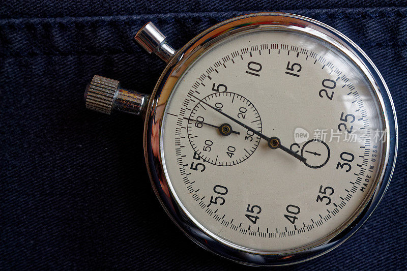 秒表在深蓝色牛仔裤的背景下，值测量时间，旧时钟箭头分秒精确计时器记录