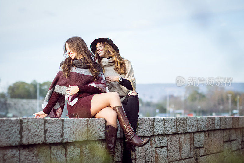 两个性感的女孩坐在城墙上，享受美好的一天