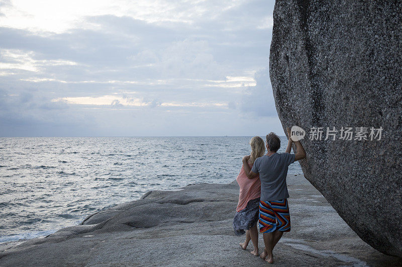 一对夫妇靠在海岸线上的巨石上