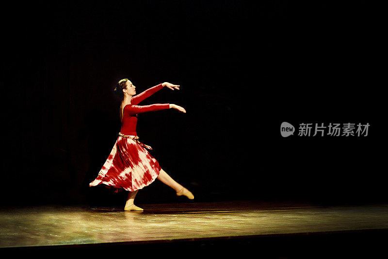 在黑色背景下，一名女子在空旷的舞台上跳芭蕾舞