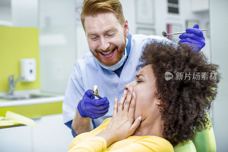 牙医在疼痛的病人面前举着拔掉的牙齿