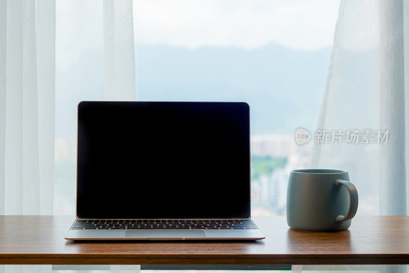 笔记本电脑放在靠窗的木桌上