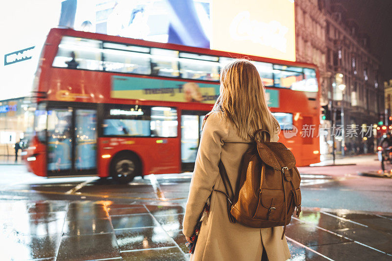 晚上，在皮卡迪利广场，一名妇女和一辆双层伦敦公共汽车
