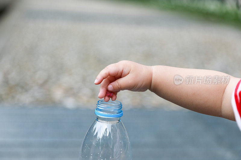 一个中国小孩的手把东西放进一个塑料水瓶的特写