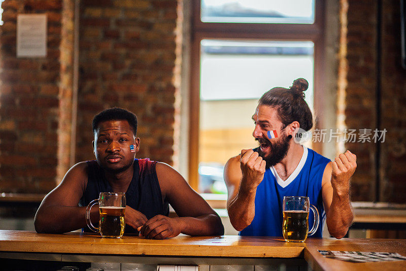 两个男人在酒吧里看篮球比赛，表现出不同的情绪