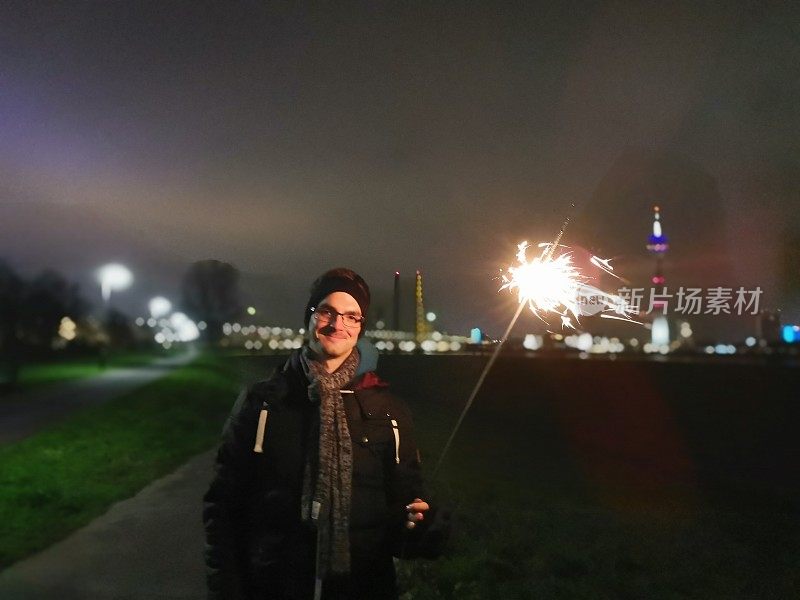 水平图像的年轻人拿着一个新年前夕的火花在Düsseldorf地平线在晚上