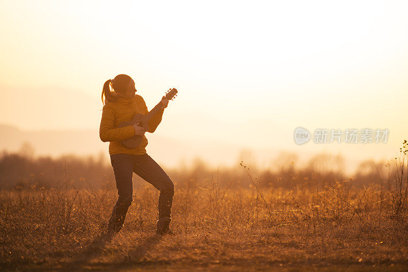 日落时分，一个年轻女子在大自然中弹吉他。剪影。