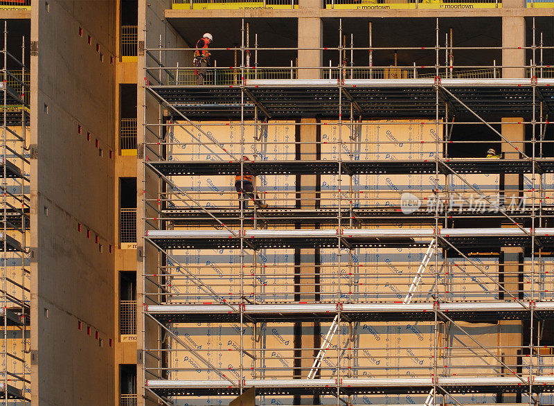 建筑工人们在一个大型现代化建筑工地的不同楼层的脚手架和平台上工作