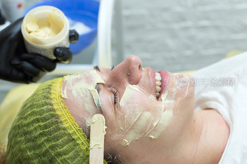 美容师在妇女脸上涂抹化妆品。