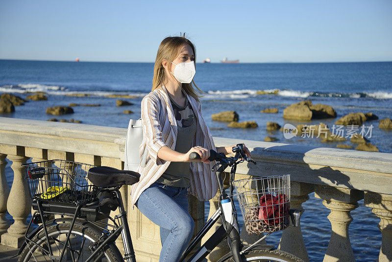 年轻女子戴着保护面罩骑着电动自行车在海边