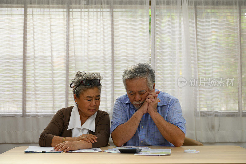 因太多的日常开支而感到悲伤或担心他们的财务状况的资深亚洲夫妇的肖像照片。资深夫妇咨询和讨论家庭开支。