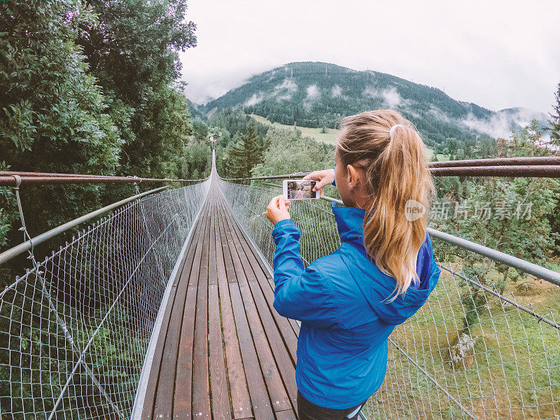 一名女子在穿过松树谷的吊桥上自拍