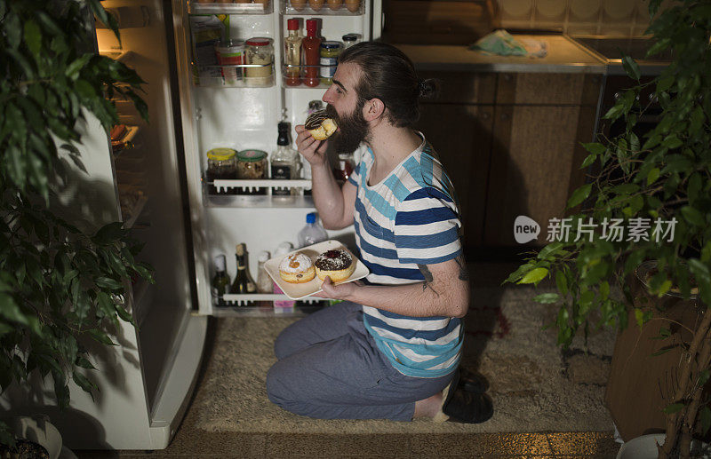 大胡子男人在冰箱前吃甜甜圈