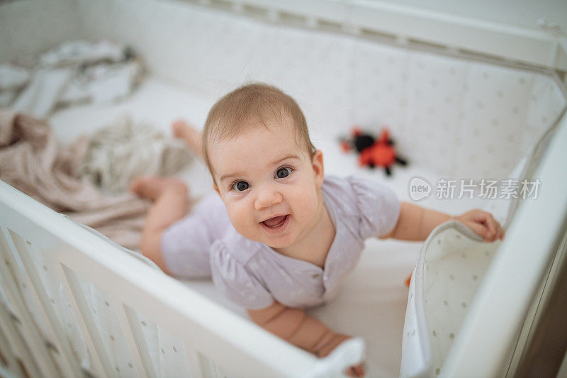 六个月大的快乐的小女孩从婴儿床上抬头看
