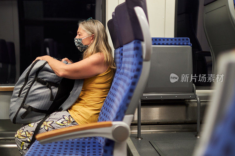 一位老人坐在火车上，腿上放着一个大行李箱，戴着防护口罩或医用口罩