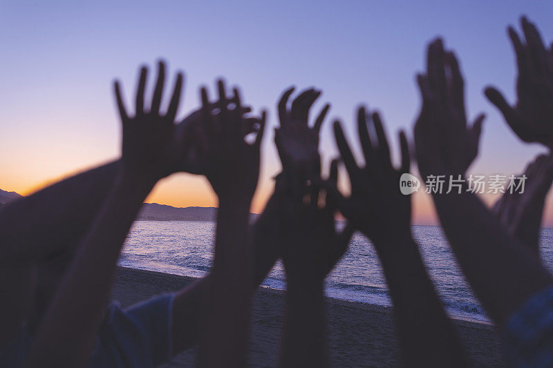 日落或日出时一群人举手的剪影。