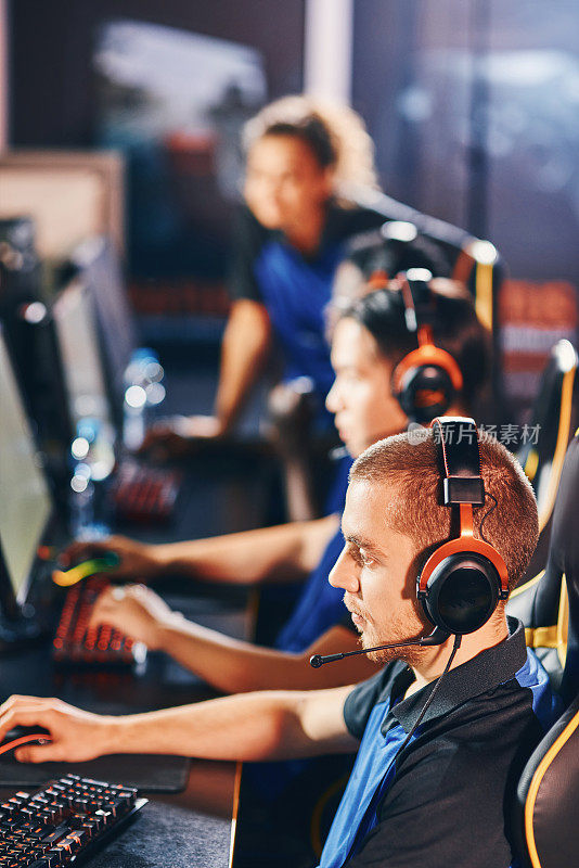 专业电子竞技游戏玩家戴着耳机坐在一排，一边参加电子竞技比赛一边玩在线视频游戏的垂直镜头
