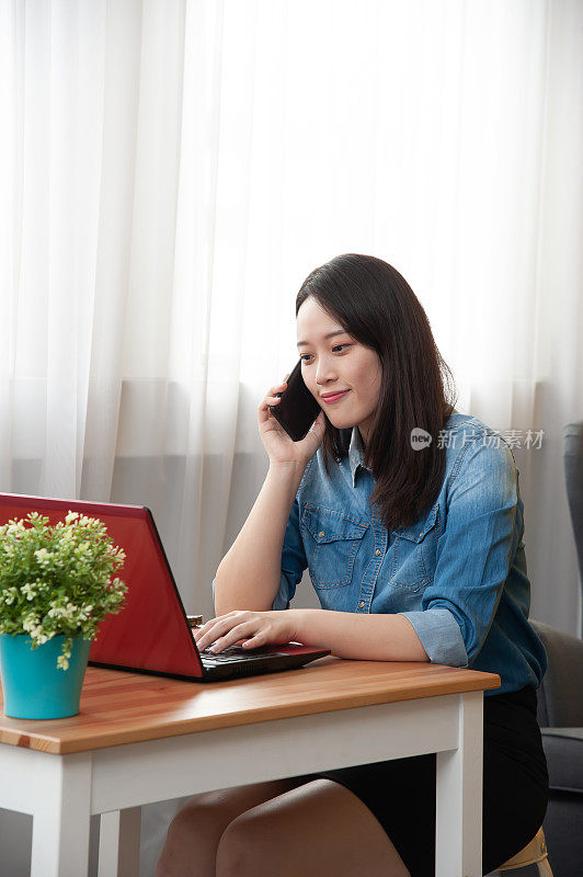 年轻的亚洲女子接听电话，而工作与笔记本电脑在她的工作站从家里。