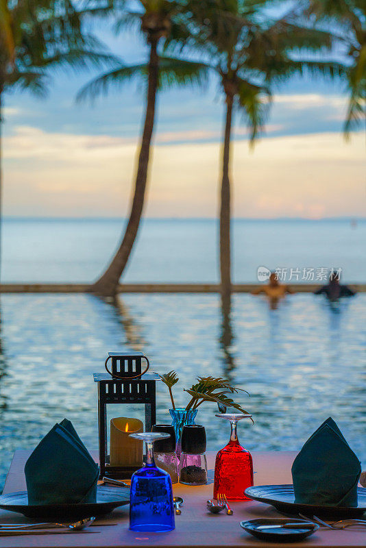 餐桌上的餐具和餐具准备晚餐在泳池边和海边的海滨精品度假村和酒店与日落天空在泰国华欣