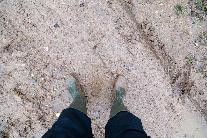 脚在绿色的橡胶靴子站在潮湿的棕色泥直接俯瞰