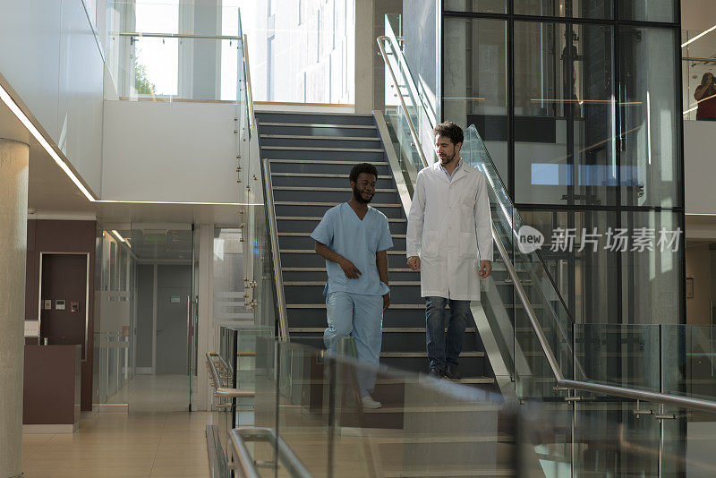 医生和黑人男护士一边走下医院的楼梯一边交谈。