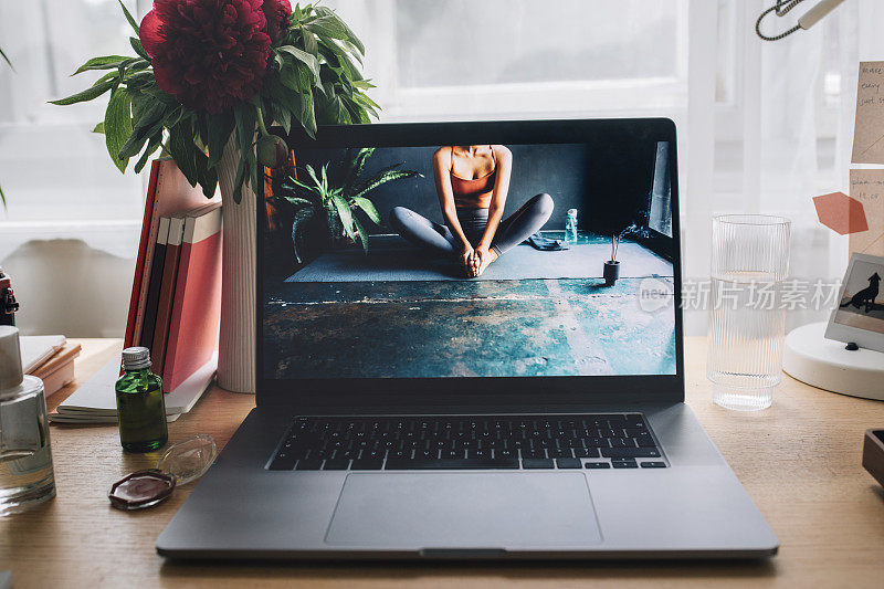呆在家里的概念:舒适的工作区域，笔记本电脑屏幕上有一张匿名女性做瑜伽的照片