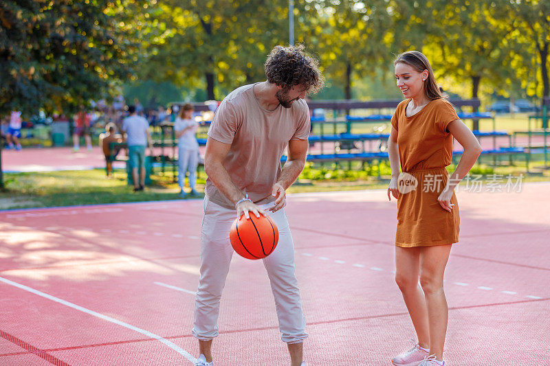 年轻人和他的妻子正在公园里玩篮球。
