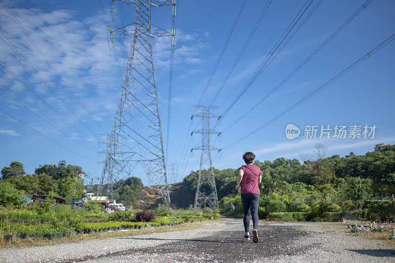 后视图亚洲华人中期成年女性与运动服跑步在早上与电力线蓝天背景