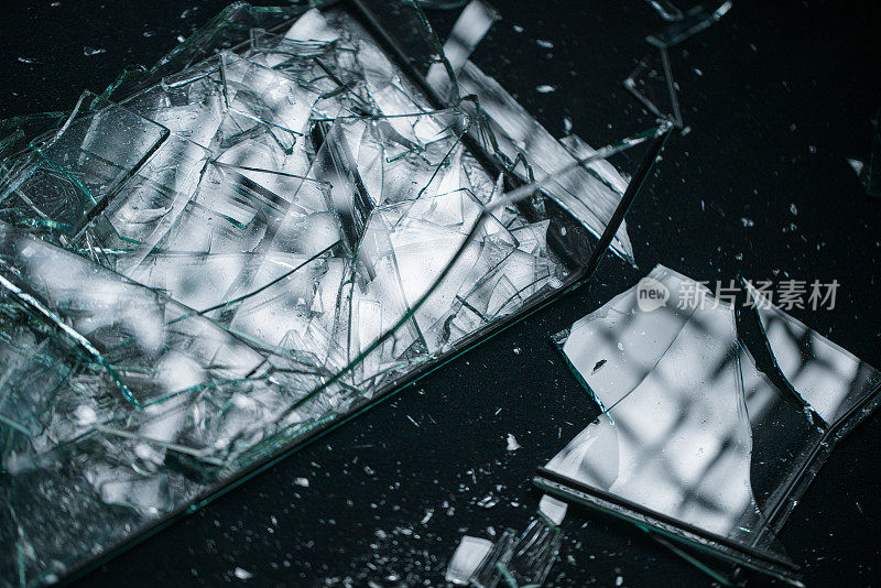 破碎的玻璃拍摄在一个工作室，专业照明在黑色背景。照相馆的黑色背景上散落着碎玻璃碎片。