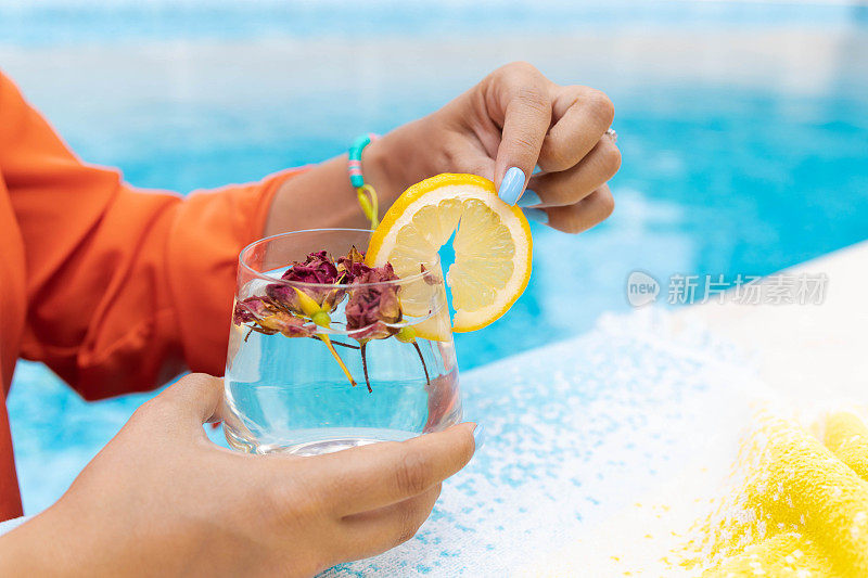 一个陌生的女人在泳池边喝水，在户外玩耍。夏季和生活方式的概念