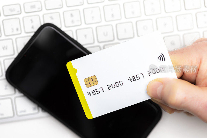 特写的网上购物者支付与智能手机上的电脑键盘与复制空间的信用卡。在线购物。