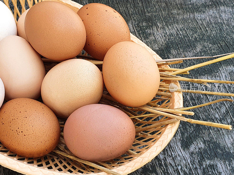家禽蛋放在篮子里，背景是旧的木质质地。天然的白色和红棕色鸡蛋。特写,俯视图。