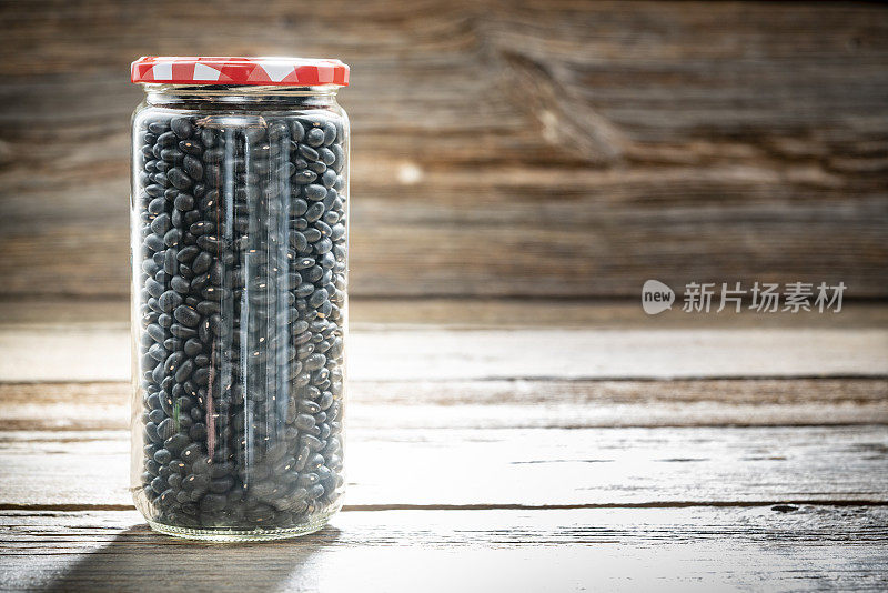 干燥的黑豆frijoles豆类在一个玻璃罐特写孤立的乡村木材