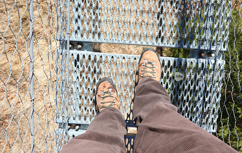 穿过悬索桥时穿着靴子的徒步旅行者的腿