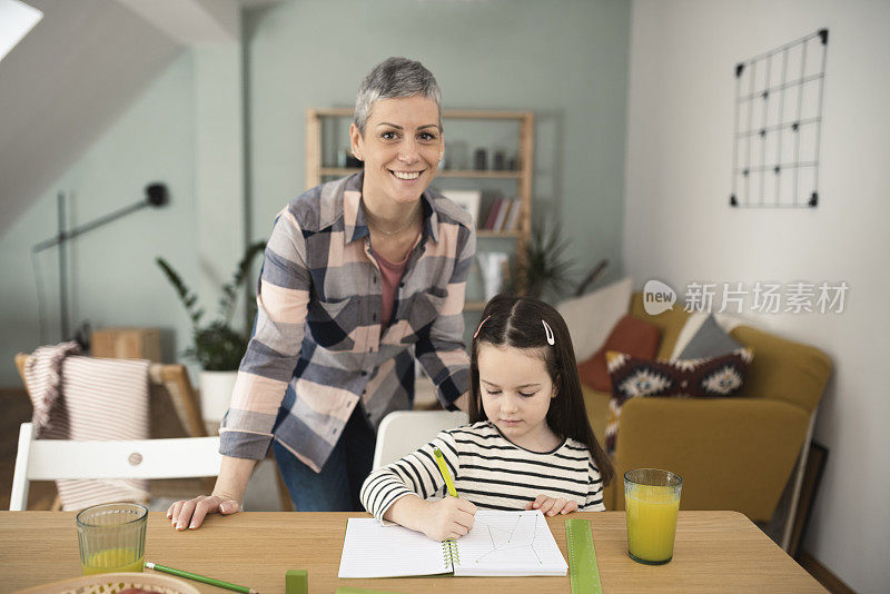 一个快乐的母亲帮助她的小女孩做家庭作业的肖像