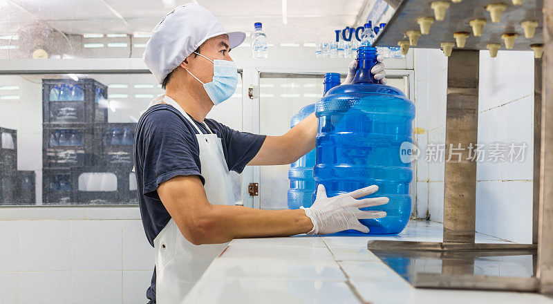 一名工人穿着工作服，脸上戴着防护口罩，在清洁饮用水工厂生产饮用水。清洁饮用水生产线