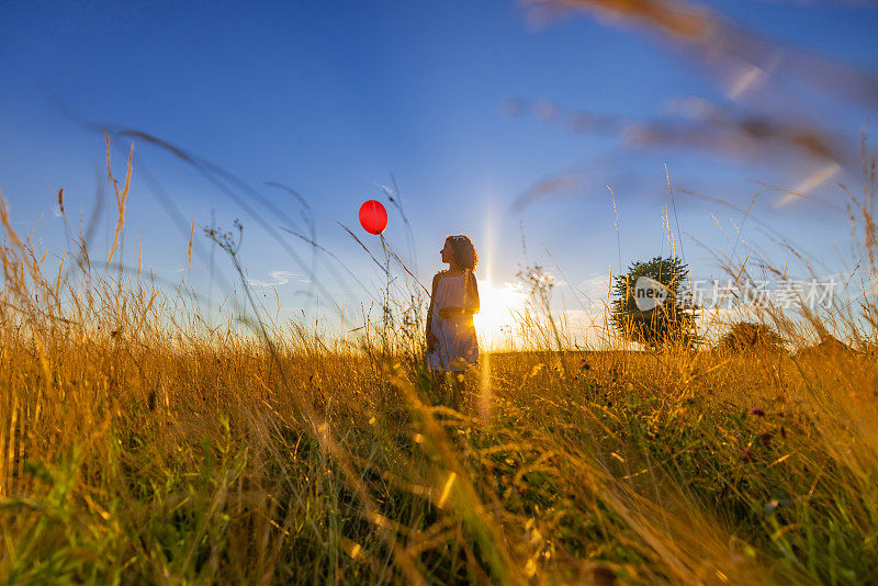 女孩在阳光照耀下站在草地上玩气球