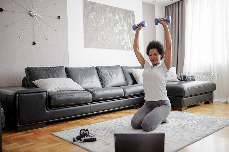 美丽的运动快乐的女人正在做举重锻炼。她正在网上看视频，并重复任务