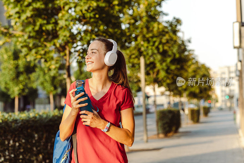 穿着红色t恤的年轻活泼的女子一边听着音乐，一边走在人行道上