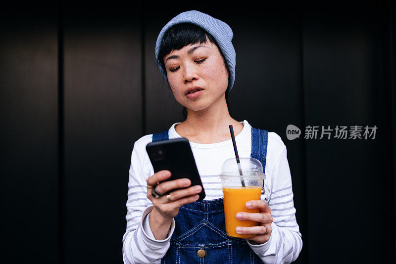 一个女人在户外一边喝果汁一边用手机