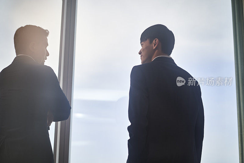 两个亚洲商人在办公室里站在窗边聊天
