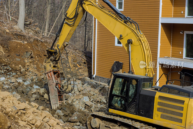 在挖掘机上使用液压锤配合手提钻，挖掘机正在粉碎一堆用于筑路的石头