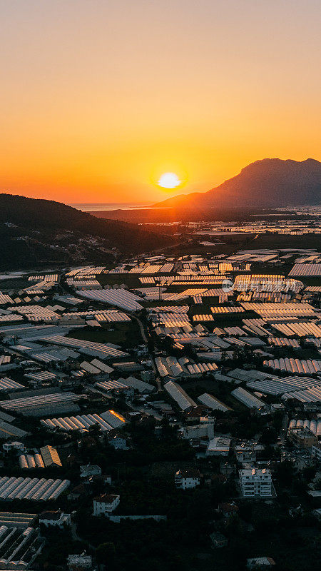 鸟瞰农场温室在广阔的土地上，在风景如画的日落在土耳其海上