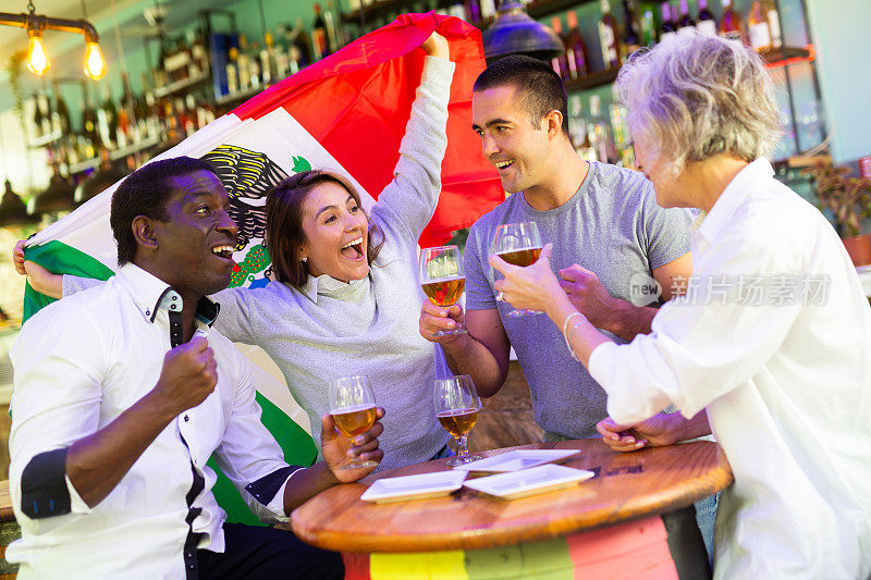 兴奋的多种族球迷挥舞墨西哥国旗，在酒吧喝啤酒庆祝胜利