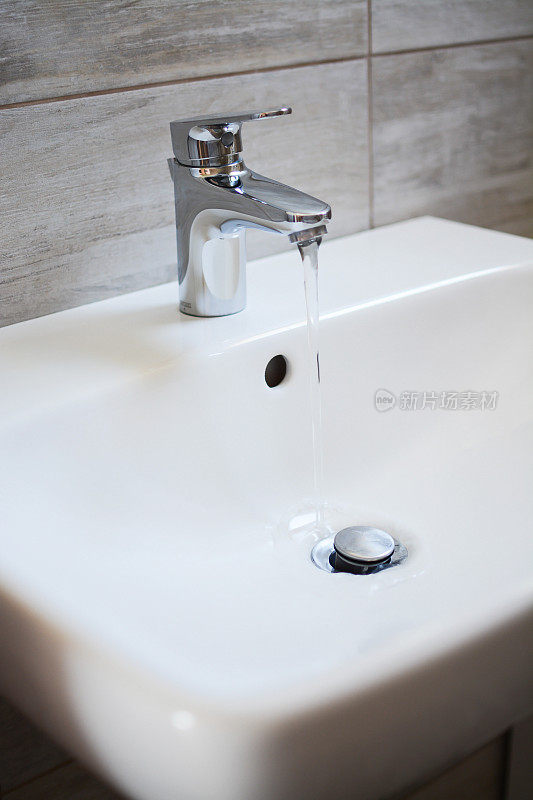 白色陶瓷水槽和镀镍黄铜金属单杆水龙头，水龙头与自来水在浴室。
