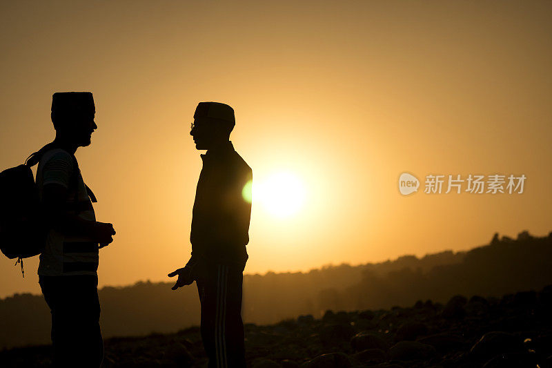 两个年轻人站在夕阳的映衬下。