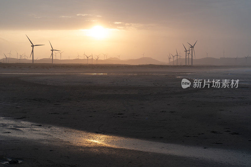 日落时海滩上的风力发电场